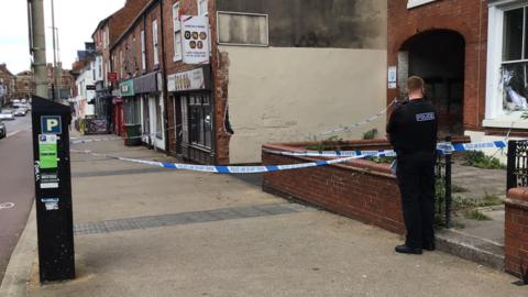 An officer standing on a cordon outside a property on a main road