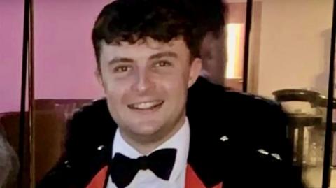 Captain Philip Gilbert Muldowney smiles as he looks into the camera, with short dark hair, wearing a dress suit and bow tie.