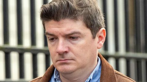 Shows a man in a blue denim shirt and brown corduroy jacket