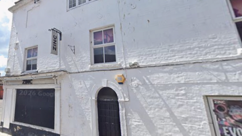 Zinc nightclub in Trowbridge - a white-painted brick building with black-out windows, posters and 'Zinc' signs, on the side of a street.