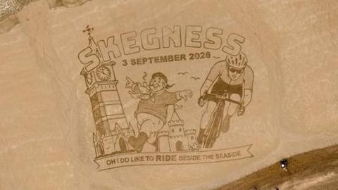 The sand art. It reads 'Skegness 3 September 2026' and depicts a clock tower, the Jolly Fisherman and a cyclist. At the bottom it says "Oh I do like to ride beside the seaside" in capital letters. 