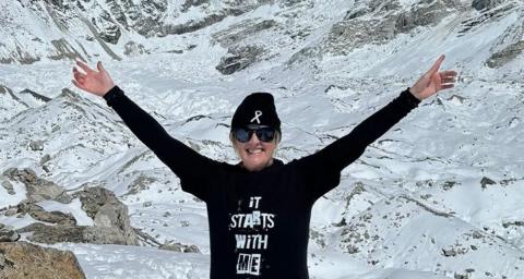 Gillian Millane at Everest base camp wearing a black top with her arms in the air