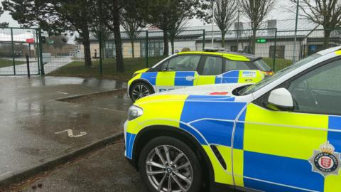 Two police cars outside a metal fence surrounding the school.