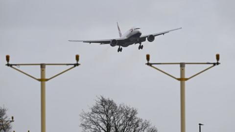 A British Airways plane coming in to land with two electrical cable structures in front of it