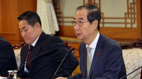 South Korea acting president Han Duck-soo wearing a dark blue suit leans forward into a microphone