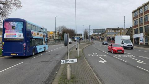 A multi-lane carriageway with a sign reading Leeds Road in the central reservation.