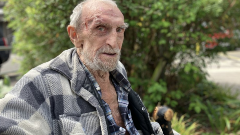 Eddie Baker wearing a checked shirt and jacket. He has white hair, a white beard and is elderly.