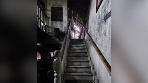 Images shows inside a pub after a fire. The open staircase, walls and both the ground and upstairs show smoke damage with daylight coming in part of the roof damaged by the blaze.