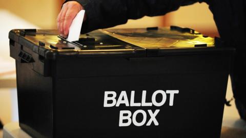 A person places a voting card into a ballot box.