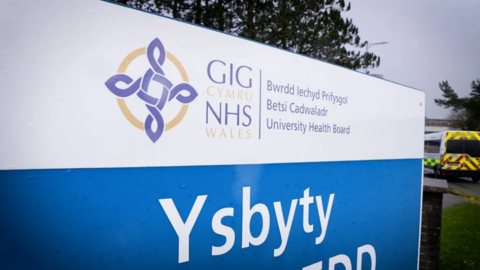 Betsi Cadwaladr University Health Board sign with an ambulance visible in the background