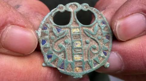 A circular-shaped brooch with detailed artwork.