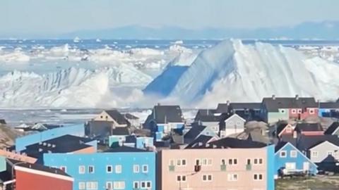 Iceberg collapsing creating wave near city with colourful houses