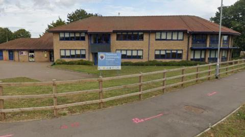 An image of Thurston Community College. It is a brick building with blue trim around the windows. A sign in front of the building says Thurston Community College. A path runs in front of a wooden fence. 