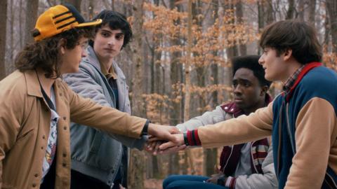 Four men putting their hands together in a scene from Stranger Things