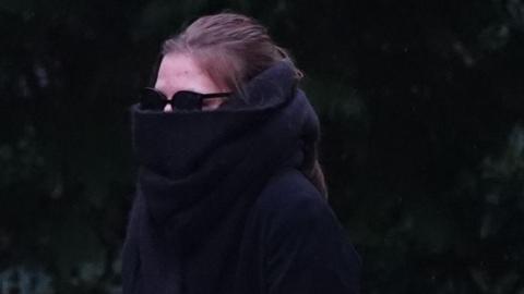 Ellis Eyles walking outside of court. She is wearing large black sunglasses and a black scarf that covers most of her face. She has brown hair which is tied back and is wearing dark clothing.