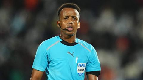 Omar Artan, wearing a blue referee's top bearing a badge reading 'Fifa Referee 2025' looks towards the camera while he is officiating a football match