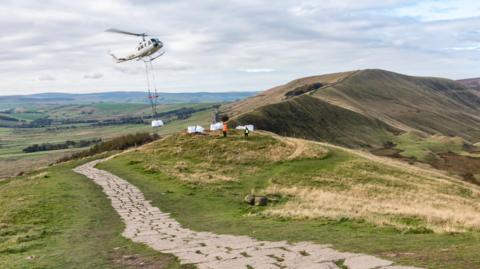 A helicopter airlifting a bag of materials to the top of a hill in the Peak District in Derbyshire 