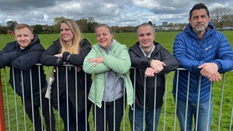 Three men and two women learning against a fence in Harlow, Essex