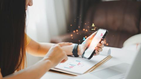 A woman looks at her smart phone. There are illustrations of notifications coming out of it. 