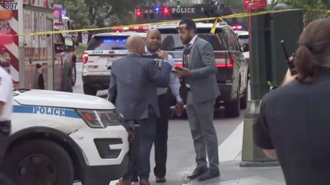 Police are standing outside the site of the Manhattan shooting, surrounded by police tape, flashing lights and vehicles.