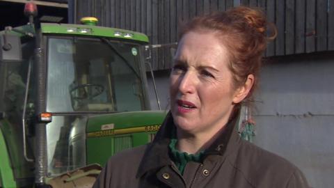 Clare Wise, a woman of about 40 with auburn hair tied back, is standing in front of a tractor.