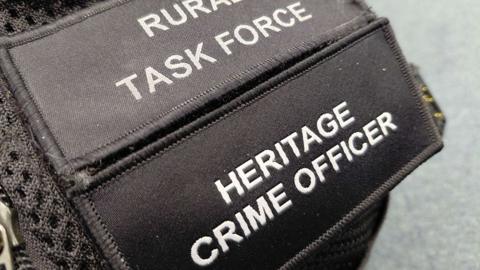 A black shoulder patch on a police officer's uniform which reads "Rural task force" and "Heritage crime officer".