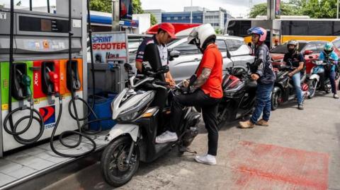 A worker helps a motorcyclist top up fuel for his bike. Behind him are more than five other bikers queuing for fuel.