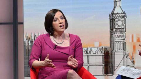Bridget Phillipson, a woman with dark hair in a bob, wearing a fuchsia pink outfit in front of a stylised graphic of the Houses of Parliament on the set of Sunday with Laura Kuenssberg