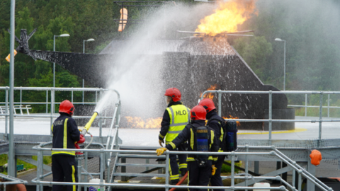 Four fire officers tackling a simulated fire on a replica helicopter