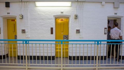 A prison officer checks behind a cell door