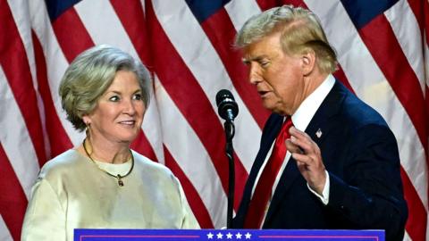 Susie Wiles (left) looks at Donald Trump (right) in front of the US flag backdrop onstage at his election night watch party in Florida on 6 November