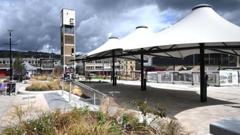 Shipley Market Square including a concrete clock tower and covered canopies with shops around the outside. 