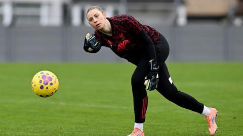 Rafaela Borggrafe rolls a yellow football while wearing black and red goalkeeper kit