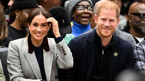 Prince Harry and Meghan sit next to each other and smile
