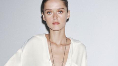 A pale model poses in a white Zara shirt staring at the camera with a blank expression and the low cut design of the top shows her protruding collarbones