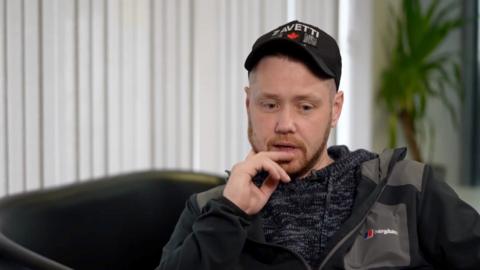 A man dressed in a grey tracksuit with a black cap on
