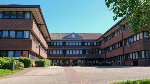 An external image of the headquarters of Gateshead Council which has a central area and two wings. It is a modern three-storey building of brown stone with a large concourse at the front.