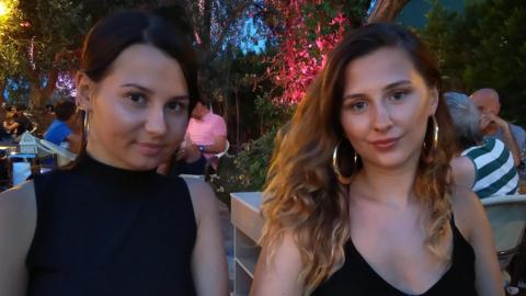 Photograph of 2 teenage girls smiling to camera. On the left, with her dark brown hair tied back, is Aimee Walton. She's wearing a black short sleeved halter neck top. On the right, with dark wavy long hair, is her older sister Adele. Adele is wearing a black tie neck top. Both have large hooped earrings.