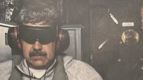 Maduro in blindfold and ear defenders after being captured
