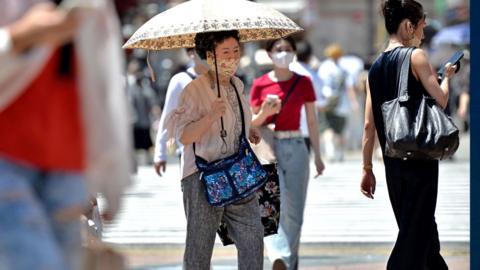 An old person walks on the street using an umbrella to protect herself from the sun on June 27, 2022, in Tokyo's popular Shibuya district in Tokyo, Japan