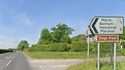 Road junction with signs on a grass verge to the right.