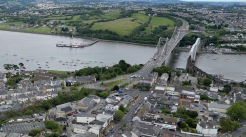 A view of the Tamar Bridge, which crosses over a river. Housing and fields are visible.