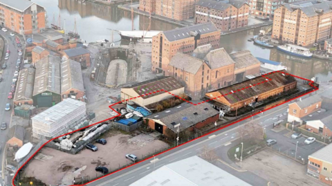 A birds eye view of Gloucester Docks, showing lots of large red brick warehouses. There is a red outline around a site with two buildings and a carpark, signalling where the new development would be. 