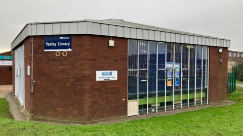 The outside of Yaxley Library – a brown, brick building with a section of long windows