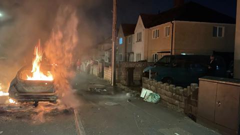 A car burns after it has been set on fire in a dark residential street