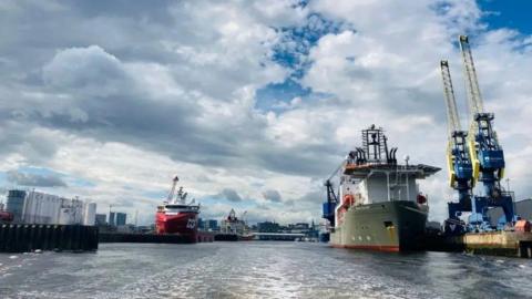 An image of large vessels in the water of Aberdeen harbour, with the city skyline in the background.