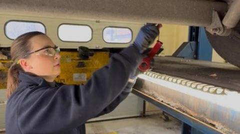 Charlotte Stanford works under a London Ambulance Service vehicle in the workshop. 