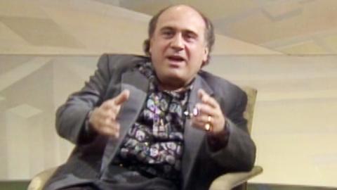 Actor Danny DeVito gesticulating with his hands while wearing a grey suit on the set of Wogan