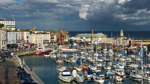 Boats in a harbour. Buildings on the side of the harbour.