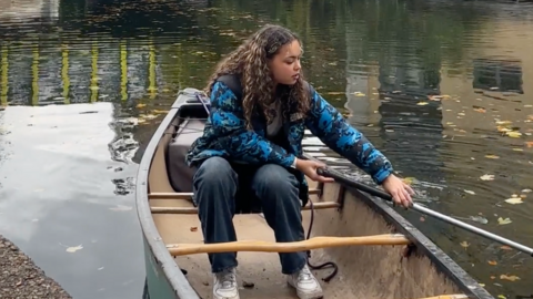 Chloe Edwards is sat in the canoe, the shot is taken quite close up. She is trying to paddle backwards.